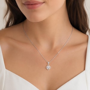 May include: A silver-toned necklace featuring a delicate chain and a pendant shaped like a four-petaled flower. The centre of the floral pendant is set with a single, clear, round-cut stone that catches the light, creating a bright, reflective appearance.