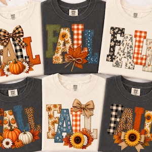 Peut inclure: Six t-shirts à col rond en crème et gris anthracite, chacun arborant le mot FALL en grandes lettres avec des motifs variés comme l'imprimé léopard, le tartan et les fleurs, agrémentés de citrouilles, tournesols et nœuds.