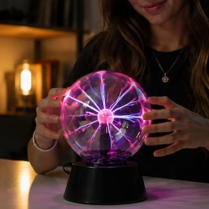 May include: A spherical plasma ball lamp featuring a clear glass globe filled with glowing purple and blue electrical filaments radiating from a central electrode, mounted on a solid black cylindrical base with a smooth, matte finish.