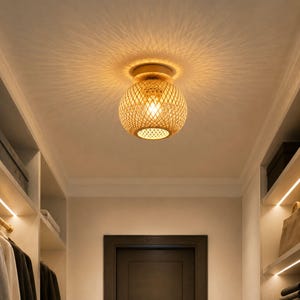 Può includere: Una lampada da soffitto sferica a incasso con un paralume in bambù intrecciato color beige naturale. La luce emette un bagliore caldo, proiettando complessi motivi d'ombra radianti sulla superficie del soffitto circostante.