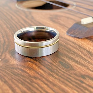 May include: A silver and gold wedding band with a thin gold band around the center of the ring.