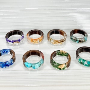 May include: Eight wooden rings with clear resin and various inclusions. The inclusions include dried flowers, gold flakes, and turquoise stones.