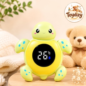 May include: A light green and yellow turtle-shaped digital thermometer with a round black display screen showing 26 degrees Celsius and a blue water drop icon. The turtle has a smooth finish, large black eyes, and small blue spots on its flippers.