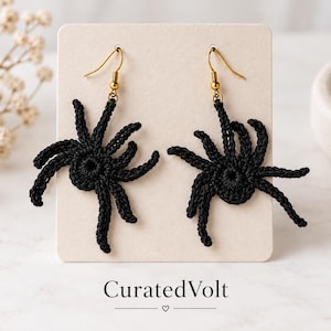 May include: A pair of black crochet spider earrings attached to a rectangular beige display card. Each spider features a circular center with eight radiating legs and is suspended from a gold-toned metal fishhook ear wire. The text CuratedVolt is printed below.