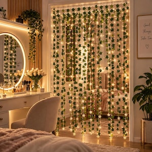 May include: A decorative curtain featuring multiple vertical strands of artificial green ivy leaves intertwined with small, warm white LED fairy lights. The strands hang down to create a glowing, nature-inspired partition for a doorway or wall.