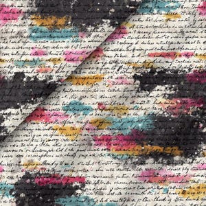 Puede incluir: Una tela con un patrón de escritura cursiva negra sobre un fondo de manchas de acuarela abstractas en tonos rosa, azul cerceta y amarillo mostaza. El diseño incluye salpicaduras de pintura blanca sobre la superficie del textil.
