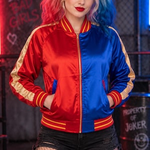 May include: A satin bomber jacket featuring a split design with a red left side and a blue right side. The jacket includes gold stripes along the sleeves, a gold front zipper, and ribbed cuffs and hem with red and yellow horizontal stripes.