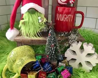 May include: A Christmas-themed display featuring a gnome with a red hat and green beard, a red mug with "NAUGHTY" text, and a collection of miniature wrapped gifts. The scene includes a small Christmas tree and a white snowflake.