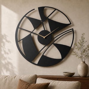 May include: A large circular wall clock featuring a black metal frame with an openwork design of geometric shapes and curved lines. The clock has a central black circular hub with two thin, gold-coloured metal hands indicating the time.