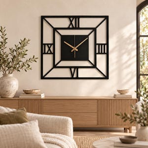May include: A square black wall clock featuring a central black square panel with gold-toned hands. The frame consists of a geometric open-work design with large Roman numerals XII, IX, III, and VI positioned at the top, left, right, and bottom.