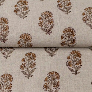 May include: A light beige fabric featuring a repeating pattern of brown floral motifs. Each motif depicts a stylized flower with multiple petals and leaves on a stem, arranged in a consistent grid across the textured surface of the material.