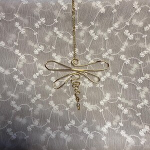 May include: A gold-toned wire dragonfly pendant suspended from a matching gold-toned chain. The dragonfly features a stylized body formed by a continuous wire loop, with two sets of symmetrical wings and a coiled wire tail ending in a small bead.