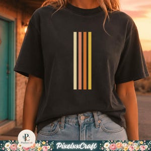 May include: A charcoal gray short-sleeve t-shirt featuring a vertical graphic design on the chest. The graphic consists of four parallel stripes in shades of cream, muted pink, burnt orange, and mustard yellow, arranged in a clean, linear pattern.