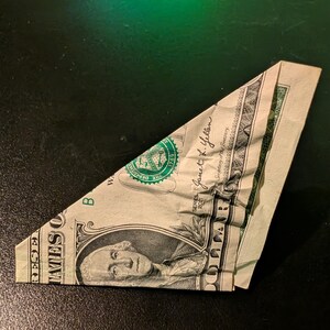 May include: A one-dollar bill folded into a triangular shape. The bill features the portrait of George Washington, the text 'THE UNITED STATES OF AMERICA', 'ONE DOLLAR', and the signature of Janet L. Yellen, with the 2021 series date visible.