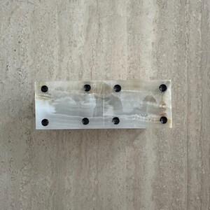 May include: A rectangular onyx domino set with black dots. The dominoes are a mix of white and tan with a polished finish. The set is displayed on a light-colored, textured surface.
