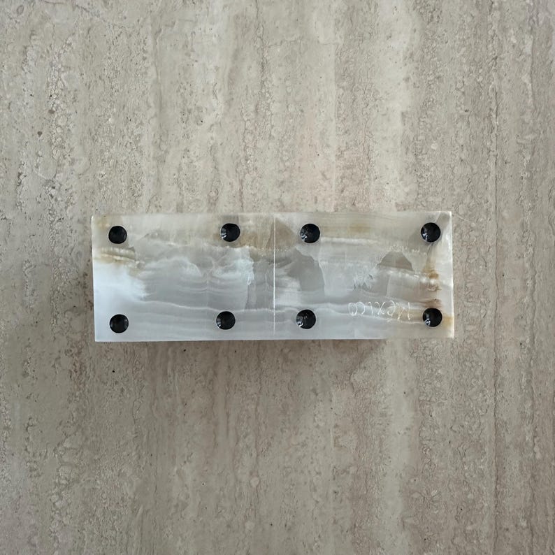 May include: A rectangular onyx domino set with black dots. The dominoes are a mix of white and tan with a polished finish. The set is displayed on a light-colored, textured surface.