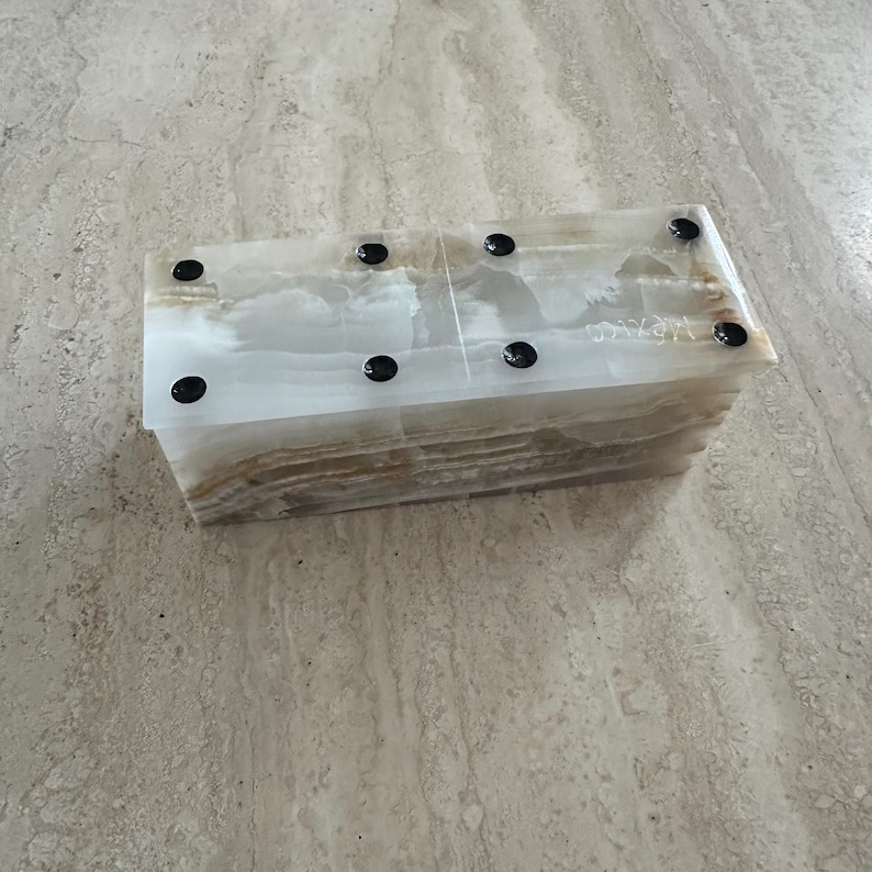 May include: A rectangular, light-colored onyx box with black circular accents. The box has a layered appearance with a marbled pattern. The word "MEXICO" is etched on the side. The box is likely used for storage or display.