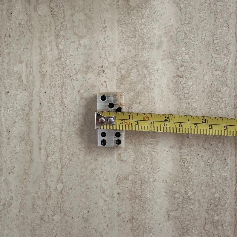 May include: A pair of silver dominoes with black dots is measured with a yellow tape measure. The dominoes are approximately 1 inch in length. The tape measure shows the measurement in inches.