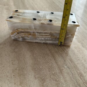 May include: A rectangular onyx box with a layered, translucent appearance. The box is approximately 4 inches tall. The top has six small, black, circular accents. The box is on a light-colored surface.