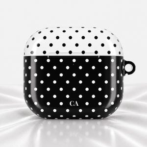May include: A glossy protective case for wireless earbuds featuring a two-tone design. The top section is white with black polka dots, while the bottom section is black with white polka dots. The letters CA are printed in white at the bottom center.