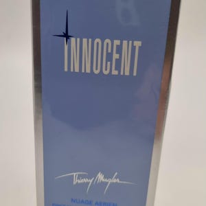 May include: A rectangular box for Thierry Mugler Innocent Nuage Aerien refillable powder brush. The box is light blue with a silver border and features a dark blue star icon, the text INNOCENT, and a net weight of 2 x 10 g or 2 x 0.35 oz.