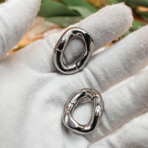 May include: Two silver-toned metal carabiner rings with a smooth, polished finish. Each ring features an oval shape with a spring-loaded gate mechanism, allowing the loop to open and close securely for attachment purposes.
