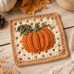 Può includere: Un quadrato all'uncinetto di tipo granny square che presenta al centro una zucca arancione tridimensionale con gambo, foglia e viticcio verdi. La zucca è centrata su uno sfondo color crema con un bordo marrone chiaro lavorato a maglia.