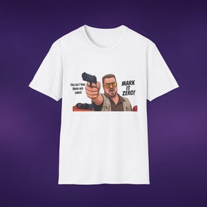 May include: A white short-sleeved t-shirt featuring a graphic illustration of a man with glasses pointing a black handgun. The text reads: This isn't Nam, there are rules! MARK IT ZERO! The design includes a bowling ball and lane in the background.
