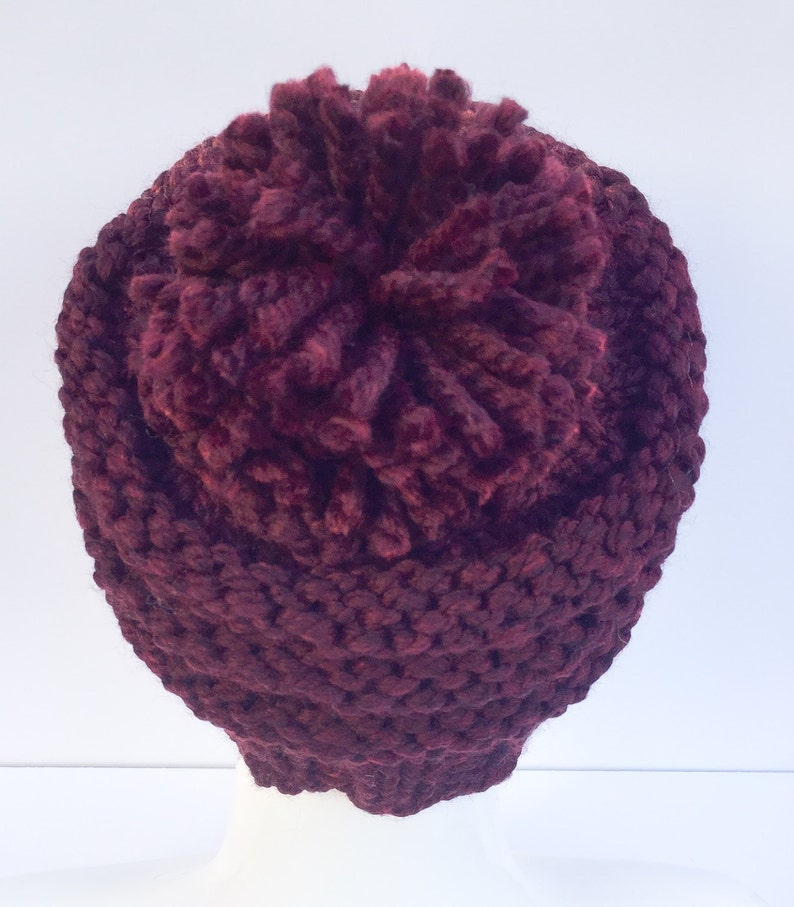 May include: A burgundy knitted beanie with a large pom pom on top.