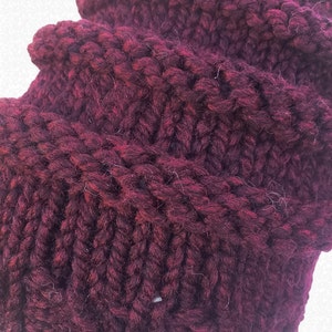 May include: Close-up of a deep burgundy knitted fabric with a textured pattern. The fabric is soft and fluffy, with a slightly fuzzy texture.