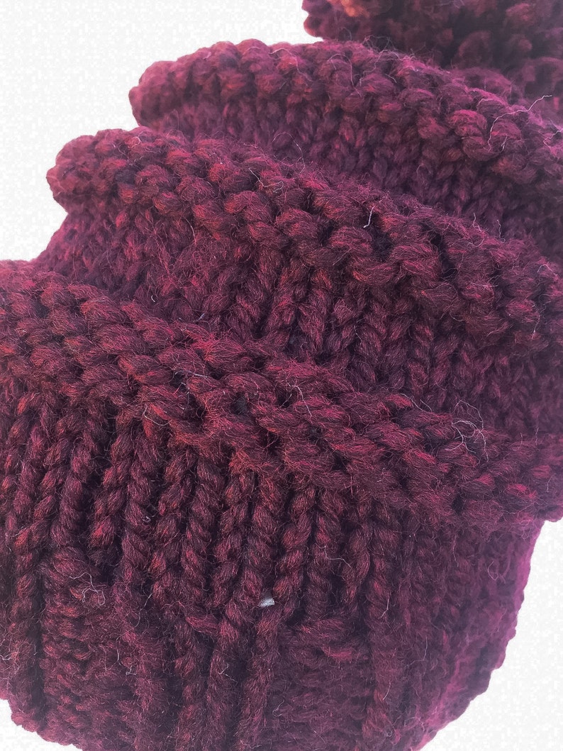 May include: Close-up of a deep burgundy knitted fabric with a textured pattern. The fabric is soft and fluffy, with a slightly fuzzy texture.