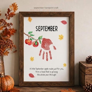 May include: A framed printable art piece featuring the text SEPTEMBER at the top, a watercolour illustration of a branch with two red apples, a red handprint, scattered autumn leaves, and the text A little September apple made just for you.