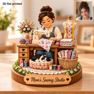 Peut inclure: Un objet décoratif imprimé à plat 2D représentant un personnage cousant à un bureau en bois avec un chat dormant dans un panier fleuri. La base comporte une plaque en bois avec l'inscription Mom's Sewing Studio et des accessoires de couture.