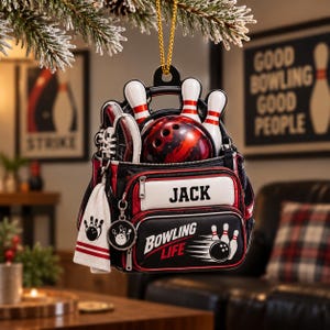 May include: A bowling-themed Christmas ornament shaped like a black and red bowling bag. It features a red and black bowling ball, three white pins, a bowling shoe, a white towel, and a circular charm. The bag displays the name JACK and the text BOWLING LIFE.