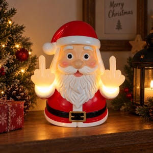 Puede incluir: Una figura iluminada de Papá Noel con gorro y traje rojo con cinturón negro, que presenta una barba y bigote blancos. La figura de Papá Noel está iluminada desde el interior y gesticula con ambas manos levantadas, mostrando los dedos corazón.