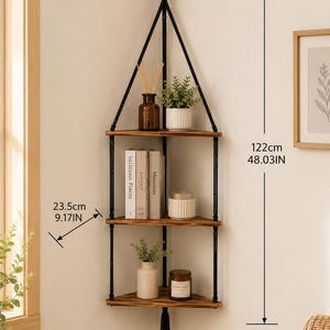 May include: A three-tier corner wall shelf with dark brown wooden boards suspended by black ropes and a wooden ring at the top. The shelf measures 122 cm in height, 32.5 cm in width, and 23.5 cm in depth, featuring a decorative tassel at the bottom.