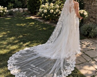 Può includere: Un lungo velo da sposa bianco con un intricato bordo in pizzo floreale. Il tessuto in tulle è ricamato con il testo "Melisse & Furkan", la data "12.12.2026" e la frase "It was always you" in filo bianco sulla parte finale.