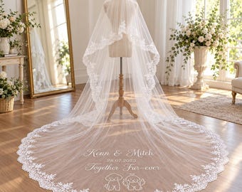 Può includere: Un lungo velo da sposa bianco con un intricato bordo in pizzo. Il tessuto è ricamato con il testo "Kenn & Mitch", la data "28.07.2025", la frase "Together Fur-ever" e due piccole illustrazioni di cani nella parte inferiore.