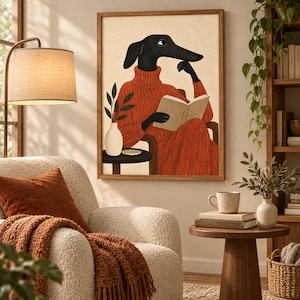May include: A framed wall art print featuring a stylized illustration of a black dog with long ears wearing a rust-colored turtleneck sweater. The dog is seated in a chair, reading an open book, with a small side table and a vase with leaves nearby.