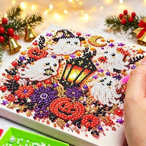 Könnte beinhalten: Eine quadratische Diamond-Painting-Leinwand mit Halloween-Motiv, bestehend aus weißen Geistern, orangefarbenen Kürbissen, einer schwarzen Laterne und violetten Blumen. Das Design besteht aus kleinen, bunten Facettenperlen in einem Mosaikmuster.