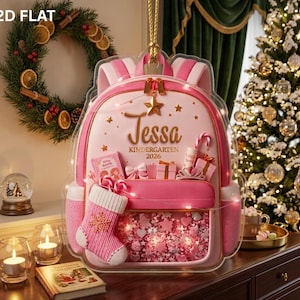 May include: A 2D flat acrylic ornament shaped like a pink backpack, featuring the name Tessa and the text Kindergarten 2026. The design includes a small pink stocking, gift boxes, a star, and a clear front pocket filled with pink confetti.