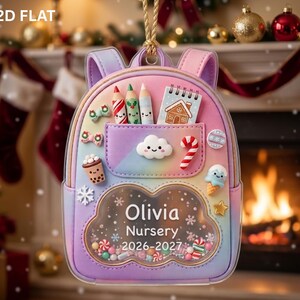 May include: A pastel gradient backpack ornament featuring a clear cloud-shaped shaker window filled with colorful beads. The text reads Olivia Nursery 2026-2027. It is decorated with miniature charms including pencils, a notebook, a candy cane, and a snowflake.