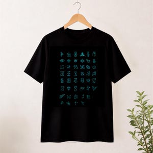 May include: A black short-sleeved t-shirt featuring a large, centred graphic print. The design consists of a grid of various geometric symbols and abstract line art characters rendered in a bright, glowing cyan blue colour against the black fabric.