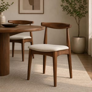 May include: A wooden dining chair with a curved backrest and a cream-colored upholstered seat. The chair features four tapered legs and a smooth, dark brown wood finish, positioned near a matching round wooden dining table.