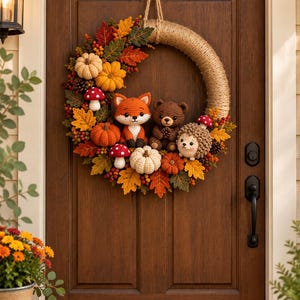 Puede incluir: Una corona circular envuelta en cuerda de yute natural, decorada con figuras de ganchillo de un zorro, un oso pardo y un erizo. El arreglo incluye calabazas, setas rojas y blancas, piñas y hojas de otoño de colores tejidas a ganchillo.