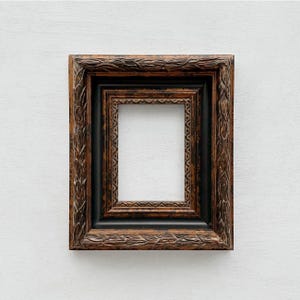 May include: A rectangular picture frame featuring a dark brown and black finish with a distressed, weathered texture. The frame has an ornate, carved leaf pattern along the outer edge and a smaller, repeating geometric border near the center.