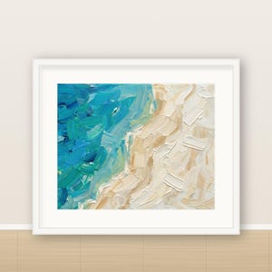 May include: An oil painting in a white frame featuring thick, textured brushstrokes of blue and turquoise ocean waves meeting a sandy beige shoreline. The artwork displays a high-contrast color palette with visible impasto paint application.