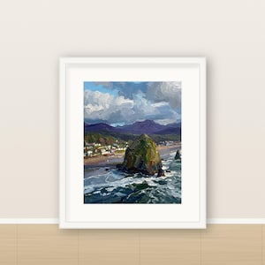 May include: A framed oil painting depicting a coastal landscape with a large green rock formation in the ocean, a sandy beach with small buildings, and dark mountains under a cloudy blue sky. The artwork is enclosed in a white frame.