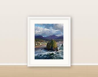 May include: A framed oil painting depicting a coastal landscape with a large green rock formation in the ocean, a sandy beach with small buildings, and dark mountains under a cloudy blue sky. The artwork is enclosed in a white frame.