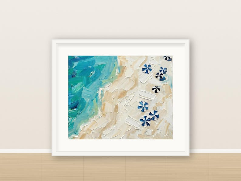 May include: An oil painting in a white frame depicting an aerial view of a beach with thick, textured brushstrokes. The scene features vibrant turquoise and blue ocean waves meeting a sandy beige shore dotted with small, blue and white striped umbrellas.